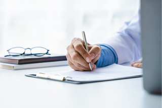 Doctor writing in a notebook with medical bottles and glasses on a desk